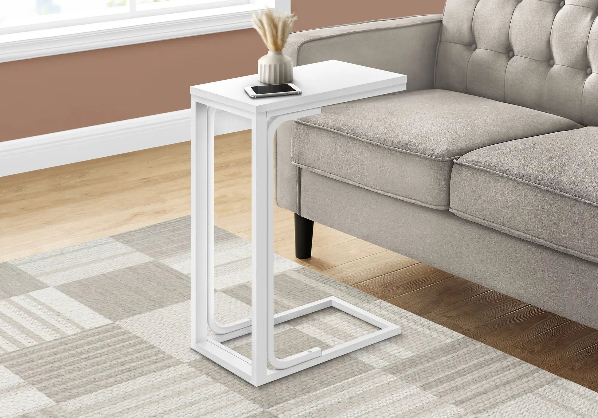C-shaped modern accent table in white with vase and smartphone beside a gray tufted sofa on Tampa Home & Garden Store