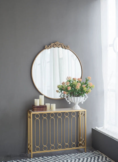 Round wall mirror with Baroque gold frame above a gold console table with candles and a vase on Tampa Home & Garden Store
