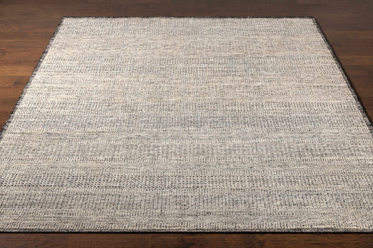 Balaclava Area Rug by Boutique Rugs in gray beige textured weave with dark border on wood floor on Tampa Home & Garden Store