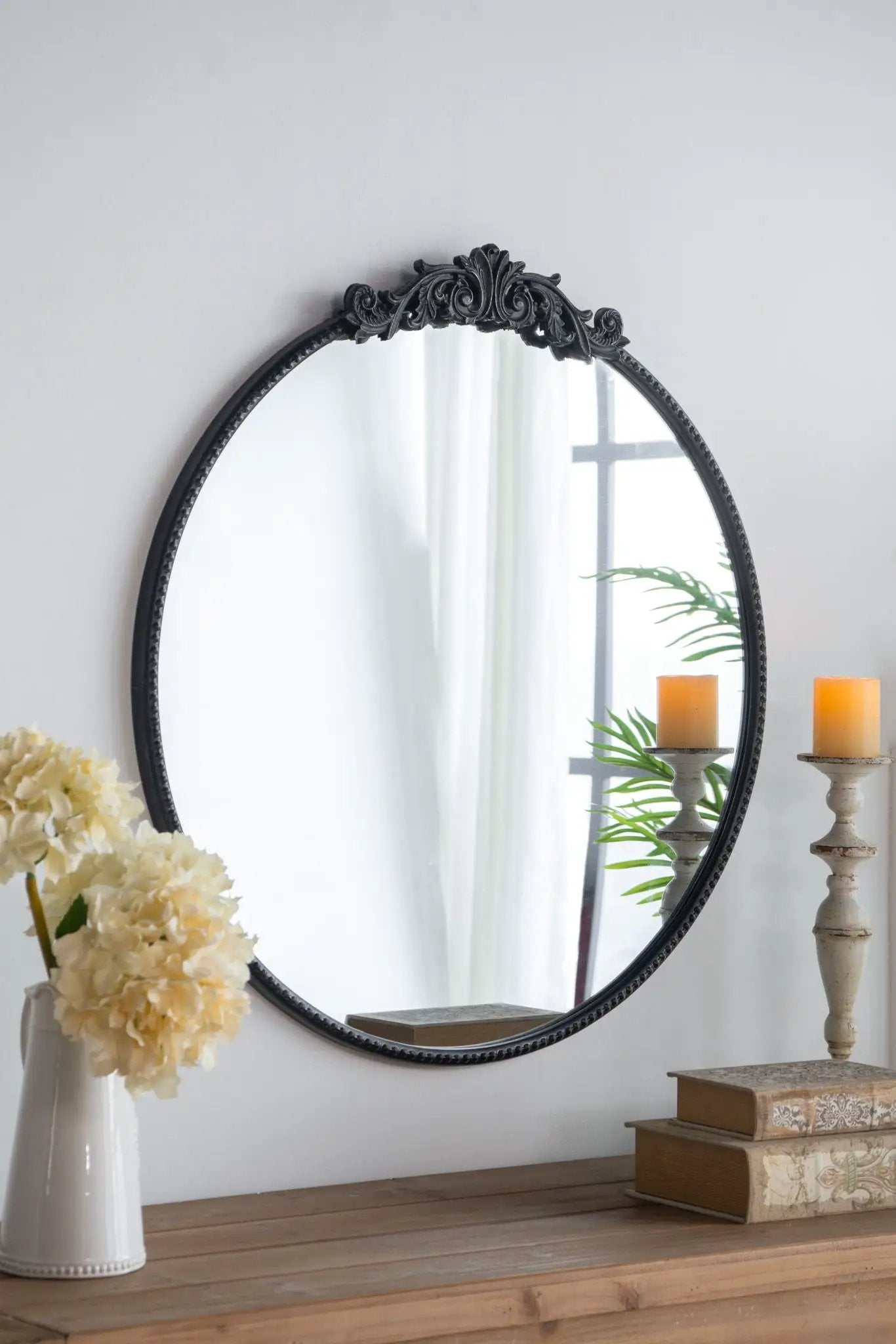 Round wall mirror with black Baroque frame leaning on a console with candles and flowers on Tampa Home & Garden Store