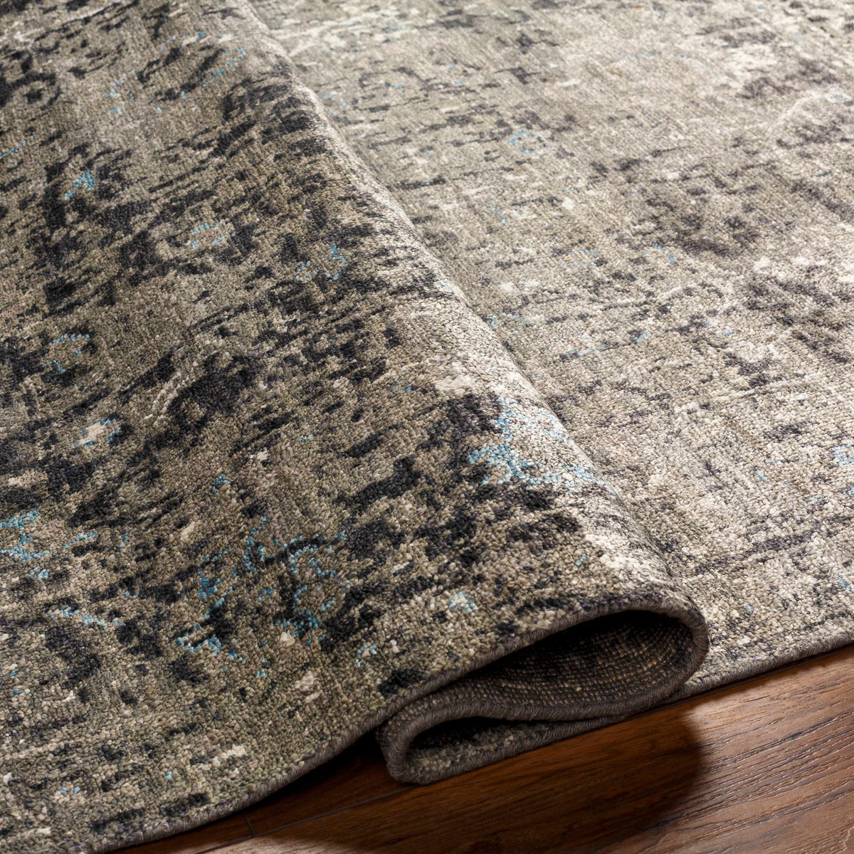 Becerril Premium Rug by Boutique Rugs in beige-brown with blue flecks, rolled edge on wood floor on Tampa Home & Garden Store