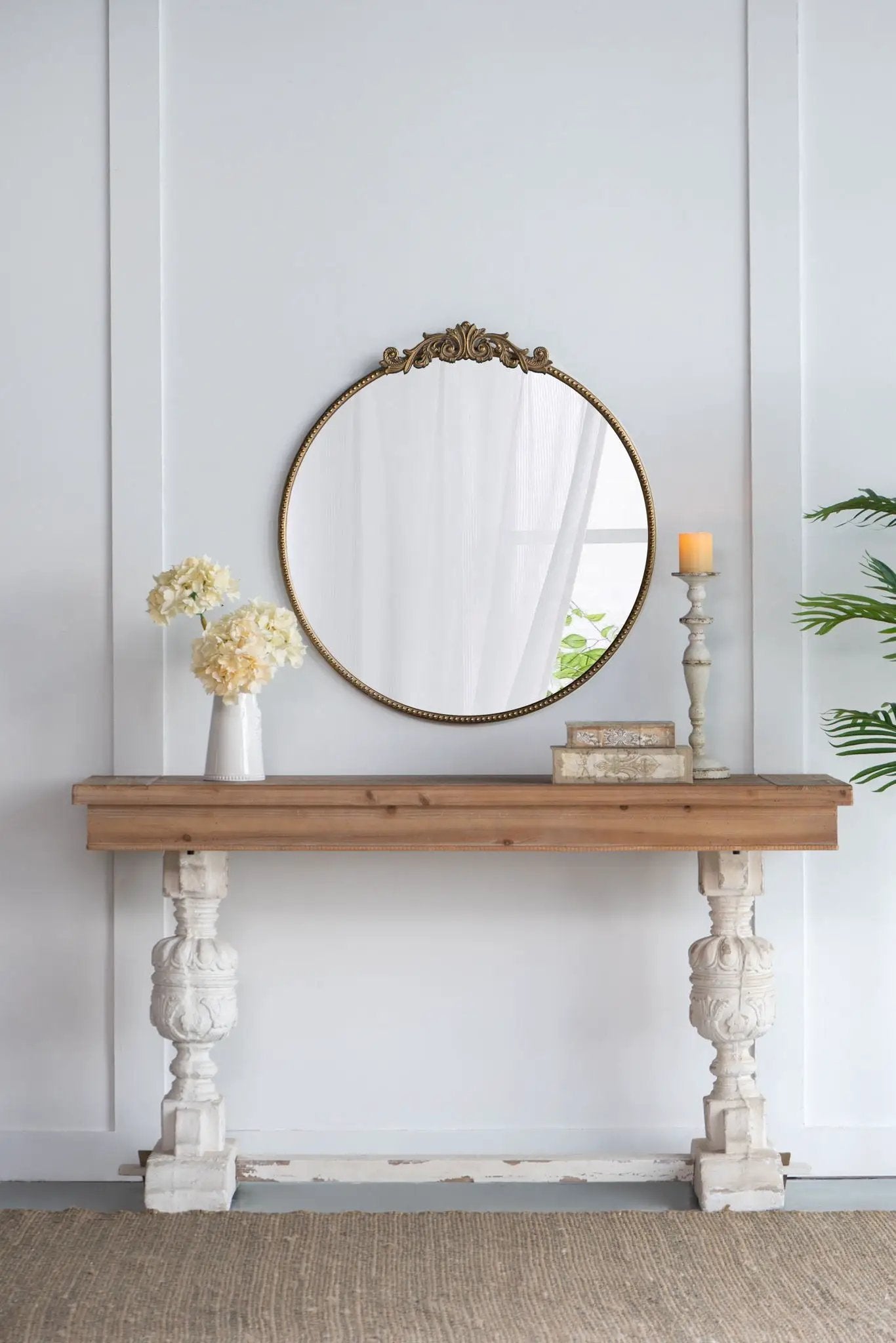 Round wall mirror with brass baroque frame and crest on a wooden console with cream flowers on Tampa Home & Garden Store