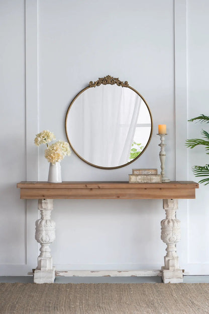 Round wall mirror with brass baroque frame and crest on a wooden console with cream flowers on Tampa Home & Garden Store