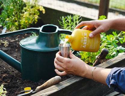 Organic Bio Insecticide by Rooted Treasures pours yellow liquid into a metal cup in a garden on Tampa Home & Garden Store