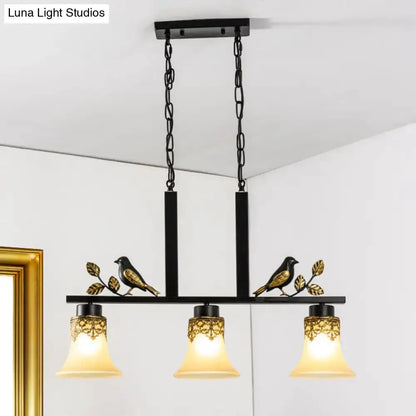 Ornate black and gold island light pendant with three tan glass bell shades and birds accents on Tampa Home & Garden Store