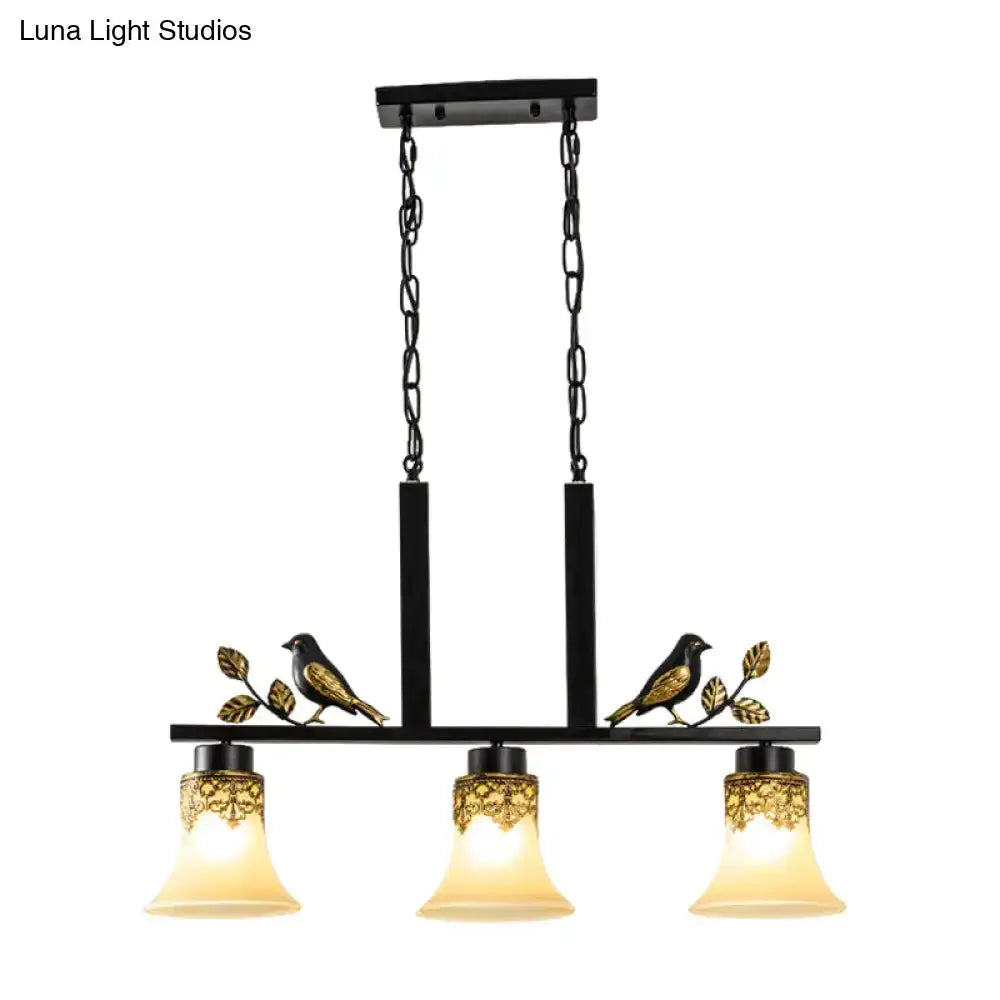 Ornate black and gold island light pendant with three tan glass shades and bird-leaf accents on Tampa Home & Garden Store