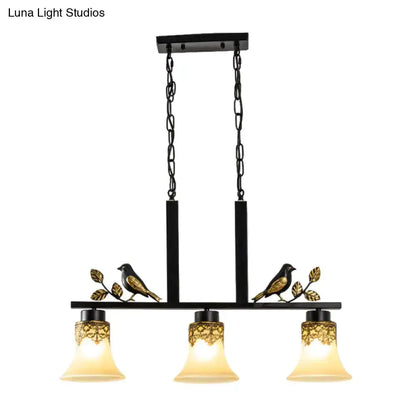Ornate black and gold island light pendant with three tan glass shades and bird-leaf accents on Tampa Home & Garden Store