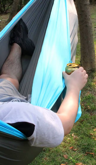 Hammock River Country Gear blue teal camping hammock, person reclining between trees with a can on Tampa Home & Garden Store