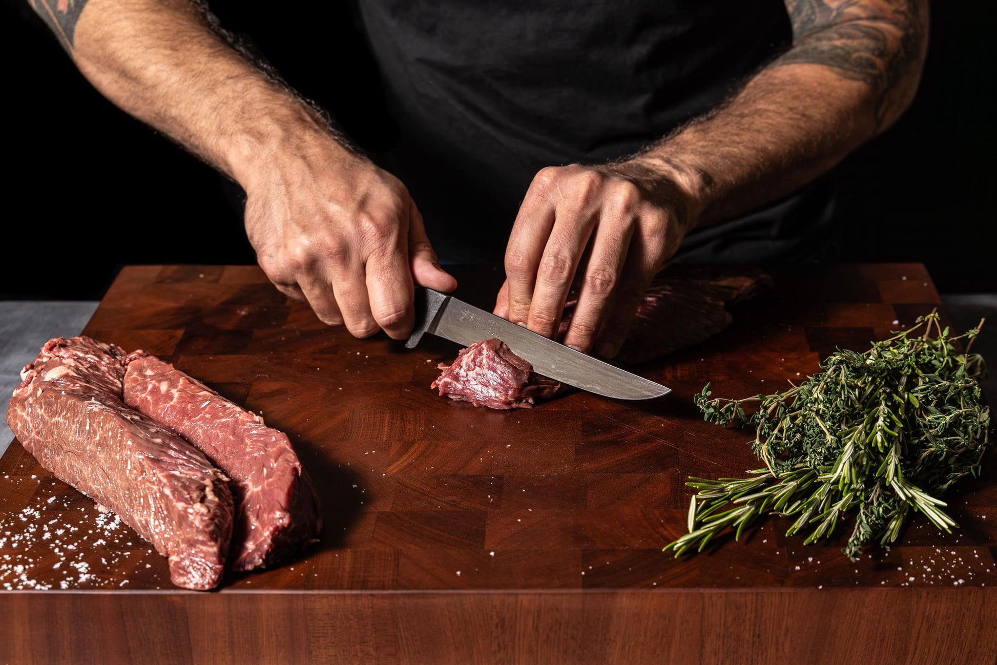 6-inch boning knife STEELPORT Knife Co. slicing meat on a wooden board with rosemary nearby on Tampa Home & Garden Store