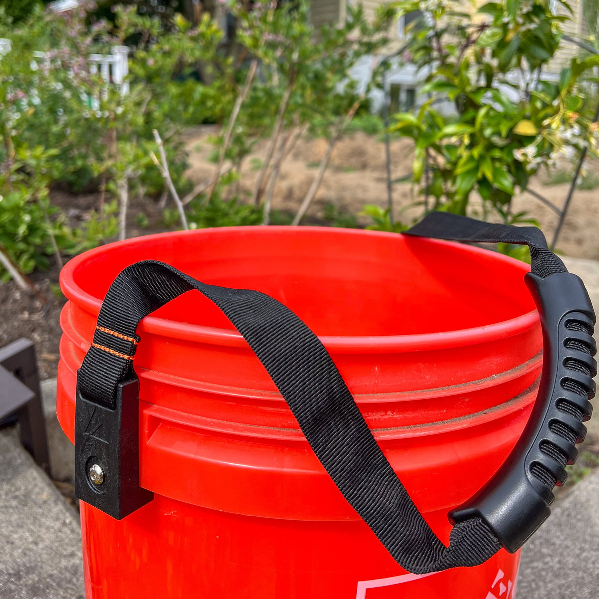 Bucket Handle by Backslope Tools; black nylon strap over a bright red bucket on Tampa Home & Garden Store