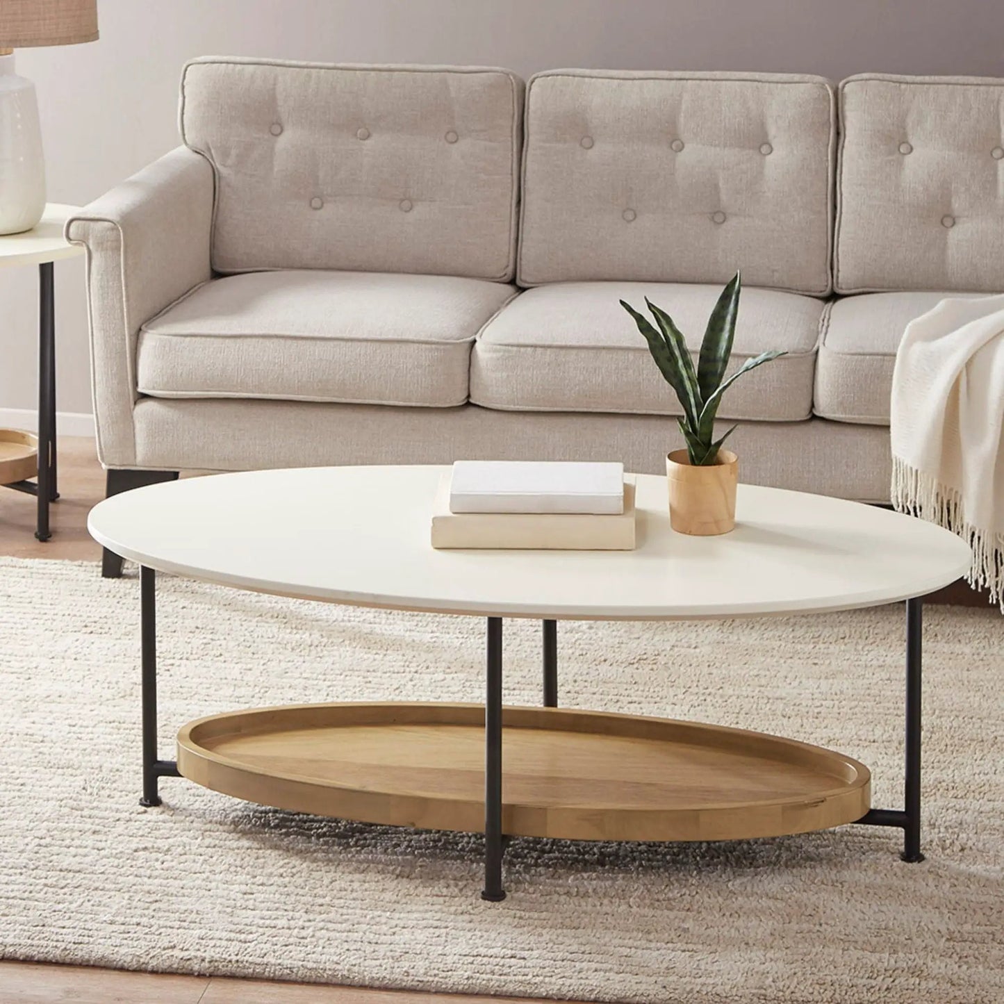 Oval coffee table with white top and natural wood shelf on black metal legs beside beige tufted sofa on Tampa Home & Garden Store