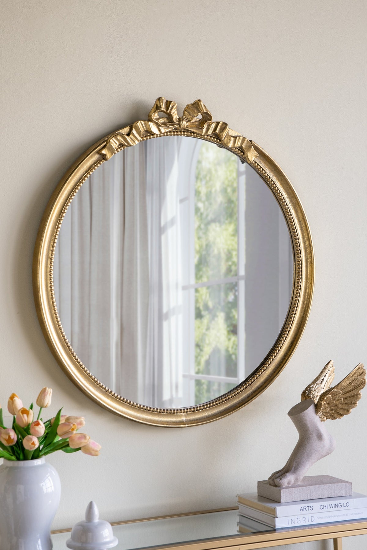 Round gold wood frame wall mirror with scroll crown above a glass console table on Tampa Home & Garden Store