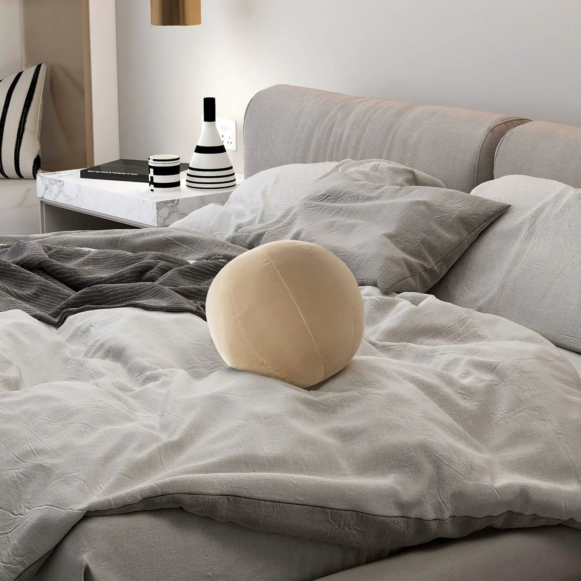 Pair of Luna Round Sphere Ball Throw Pillows on bed with gray bedding beside marble nightstand on Tampa Home & Garden Store