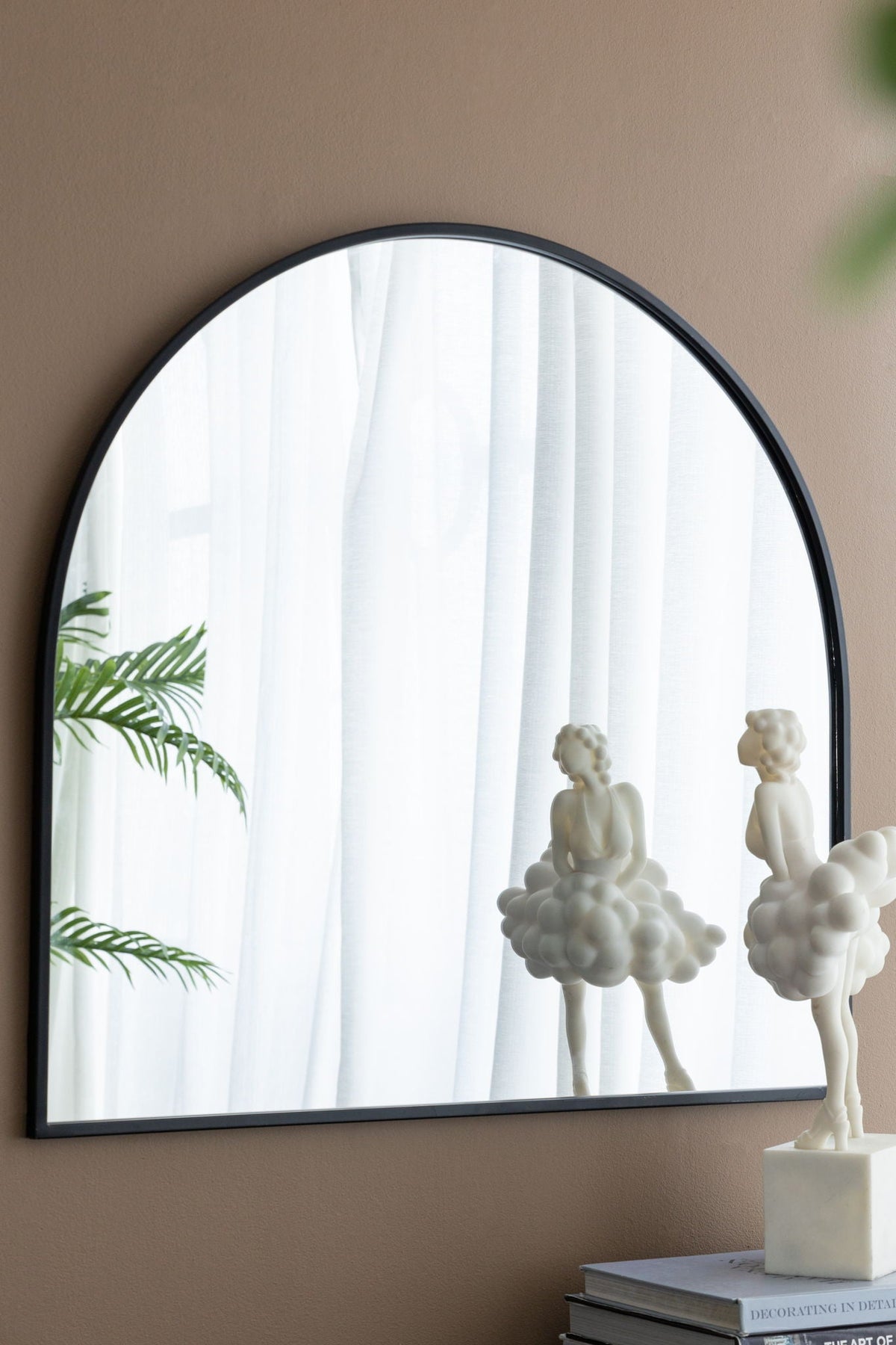 Arched mirror with black metal frame on beige wall, reflecting white curtains and plant on Tampa Home & Garden Store
