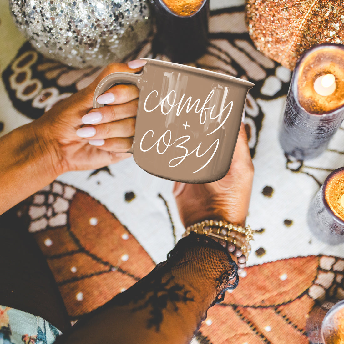 Comfy + Cozy taupe ceramic mug by Gia Roma, held by hands over a patterned rug with candles on Tampa Home & Garden Store