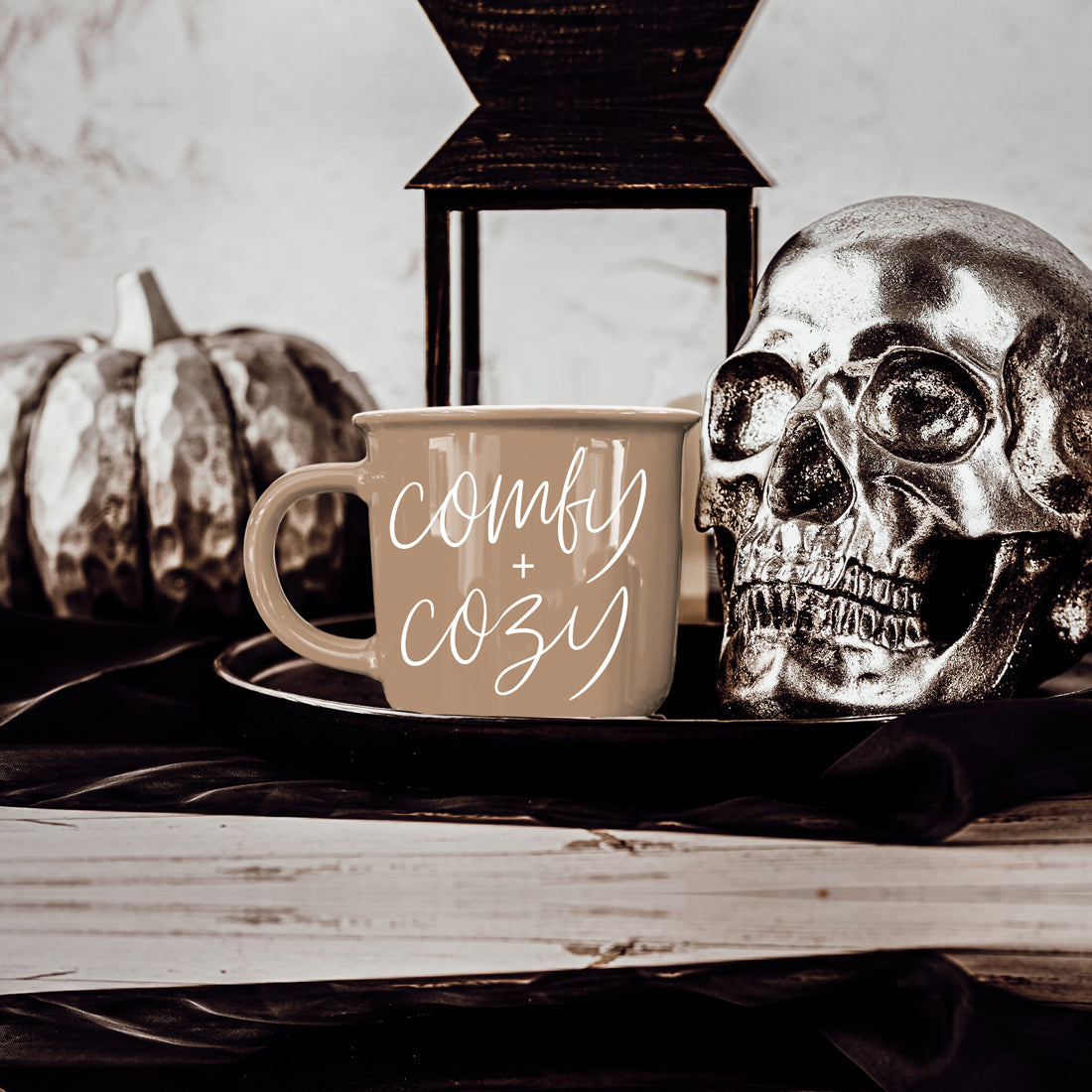 Beige ceramic coffee mug with white script comfy + cozy beside a decorative skull on a tray on Tampa Home & Garden Store