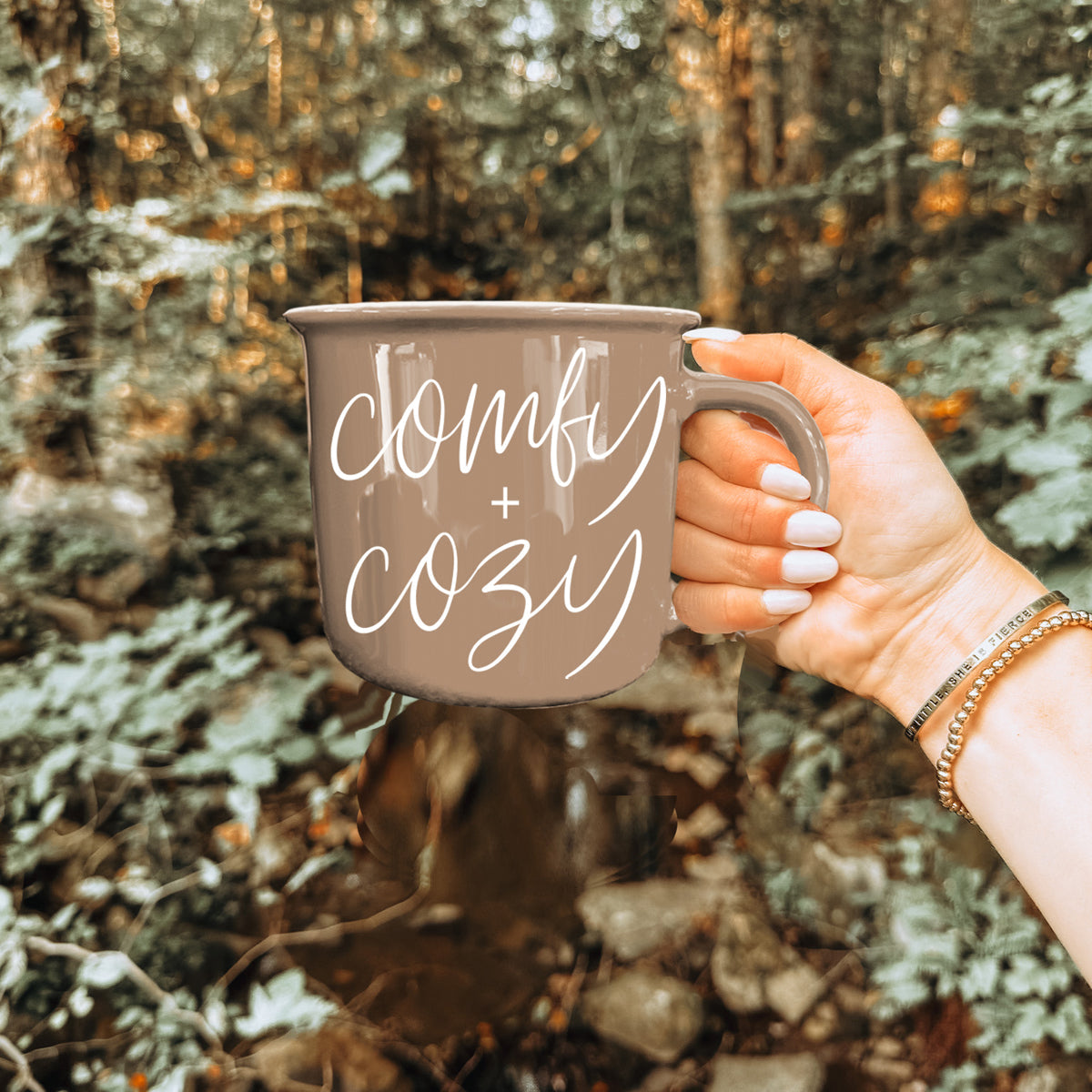 Comfy + Cozy coffee mug in taupe with white script, held by a hand outdoors on Tampa Home & Garden Store