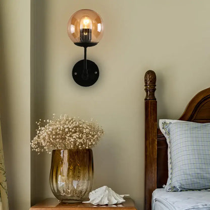 Black amber globe sconce with black metal mount lights a bedroom wall on Tampa Home & Garden Store