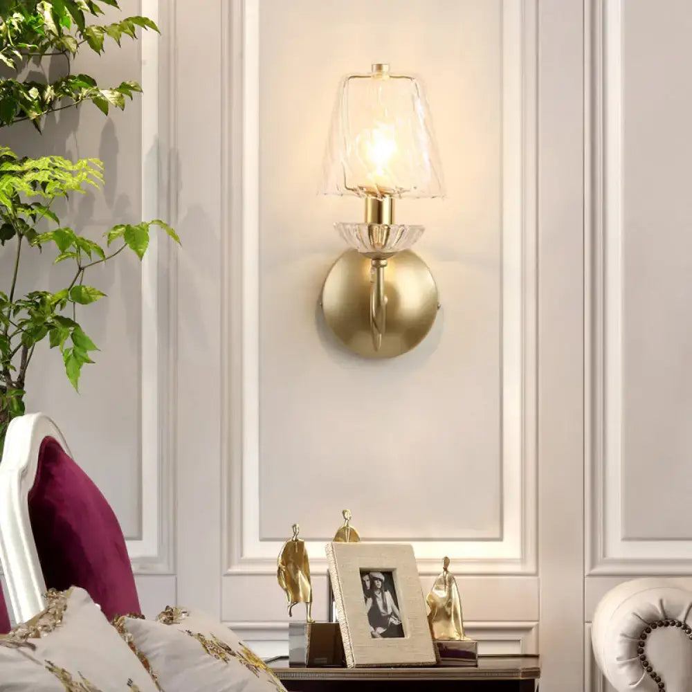 Gold swirl glass wall sconce with clear shade and brass mount lit in a bedroom on Tampa Home & Garden Store