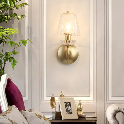 Gold swirl glass wall sconce with clear shade and brass mount lit in a bedroom on Tampa Home & Garden Store
