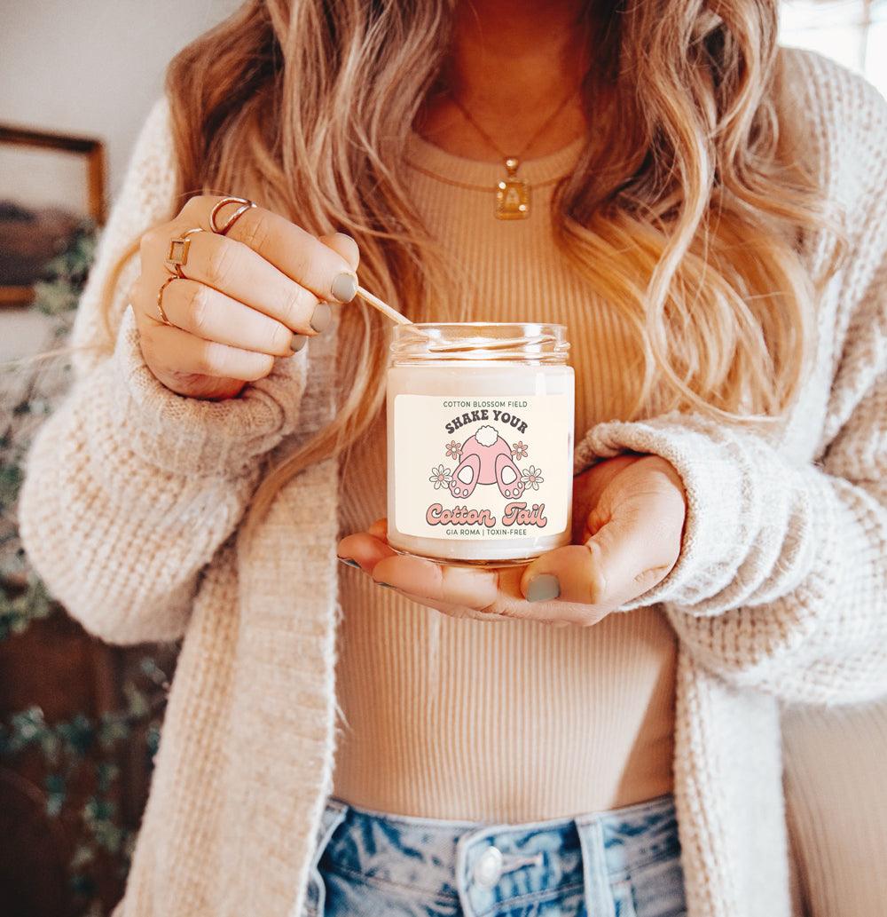Cotton Blossom Retro Candle Gia Roma in a clear glass jar with a pink label, held by a woman in a beige knit sweater on Tampa Home & Garden Store