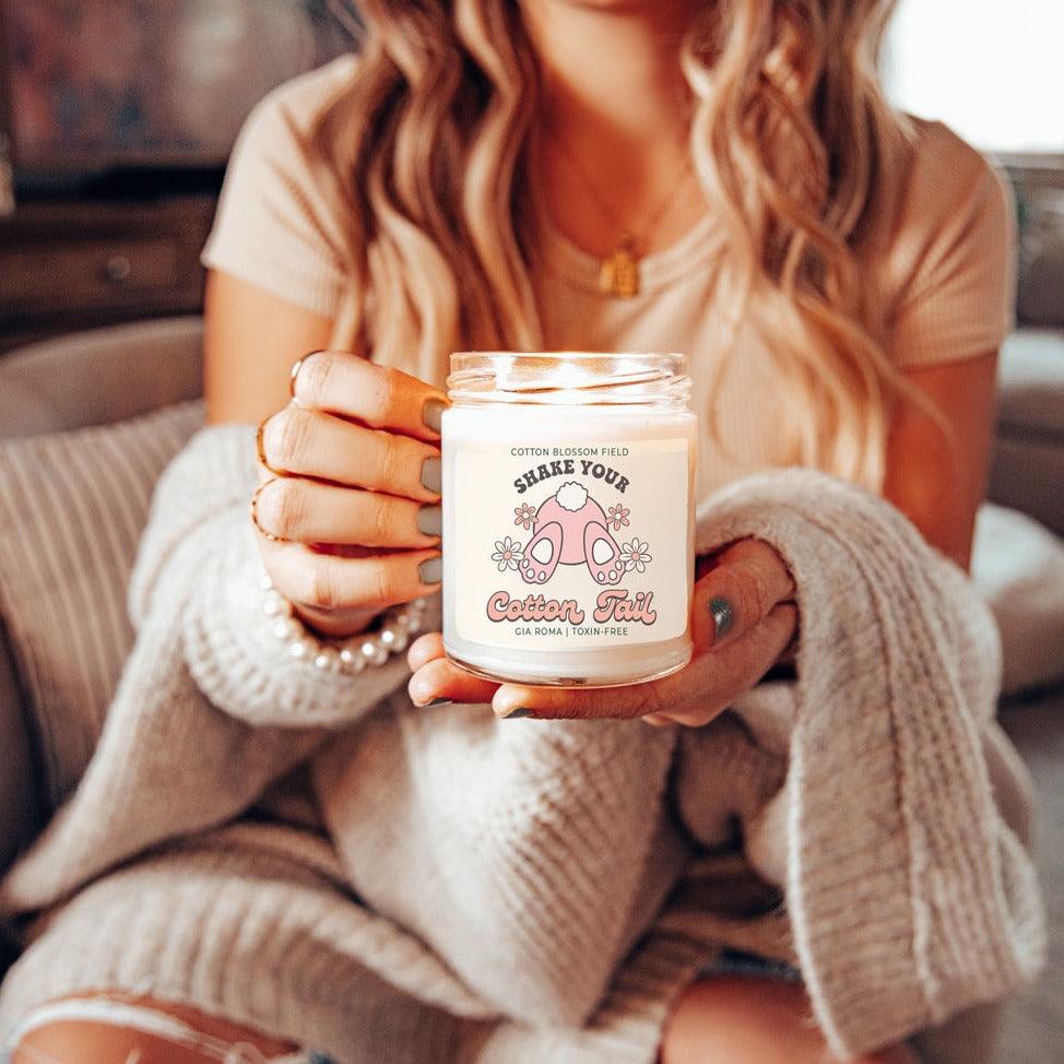 Cotton Blossom Retro Candle Gia Roma in white glass jar with pink label held by a woman in beige knitwear on Tampa Home & Garden Store