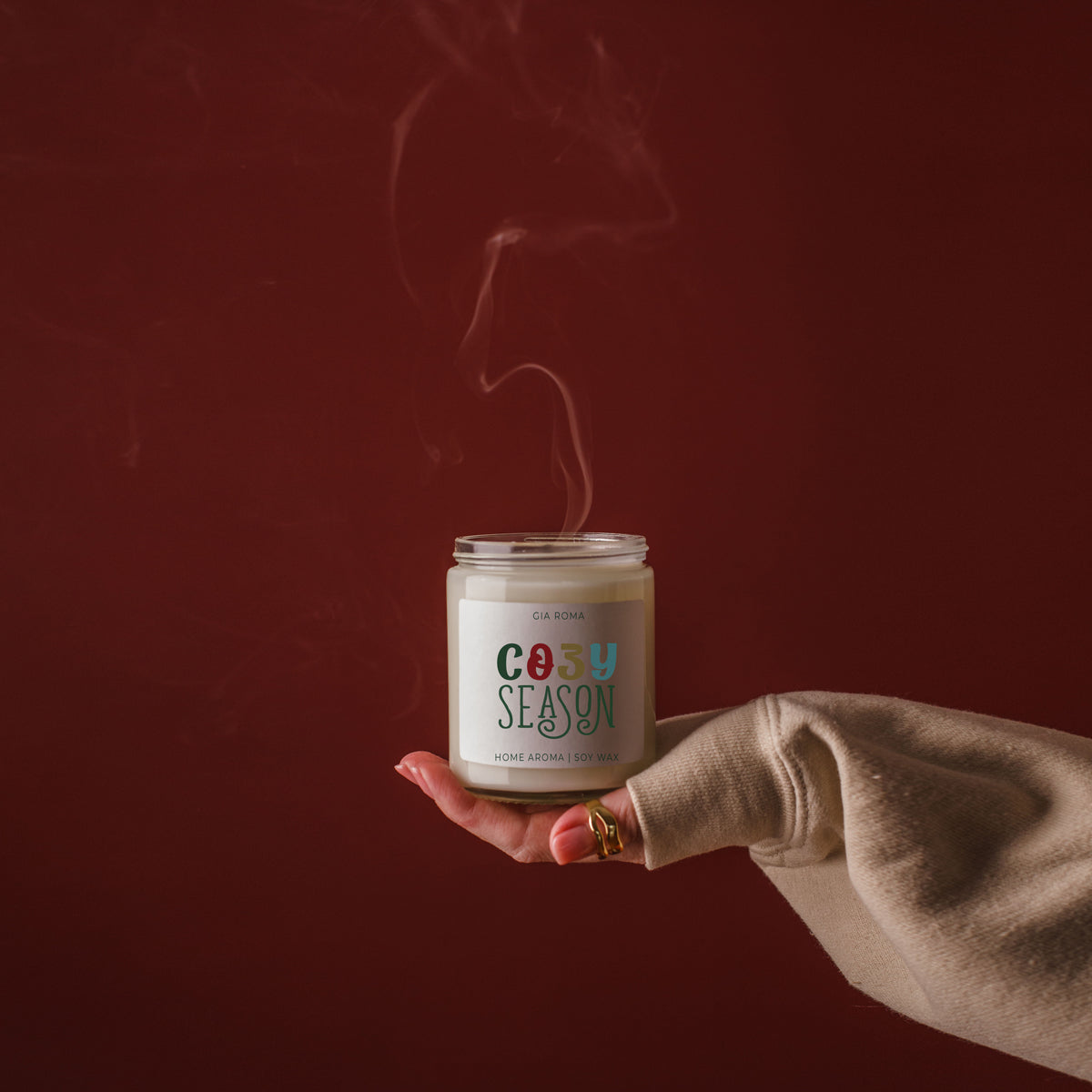 Cozy Season Candle by Gia Roma in glass jar with cream wax, held against burgundy backdrop on Tampa Home & Garden Store