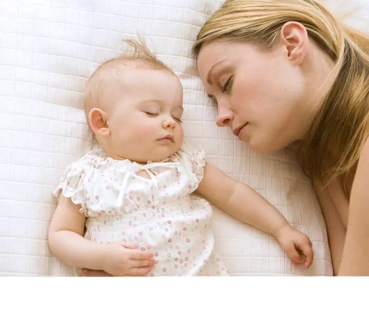 Baby pacifying sleep aid resting beside mother on white bed in white floral outfit on Tampa Home & Garden Store