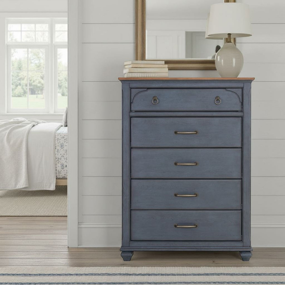 Blue accent chest by HouseOfZazla stacked with books and lamp in a shiplap bedroom on Tampa Home & Garden Store
