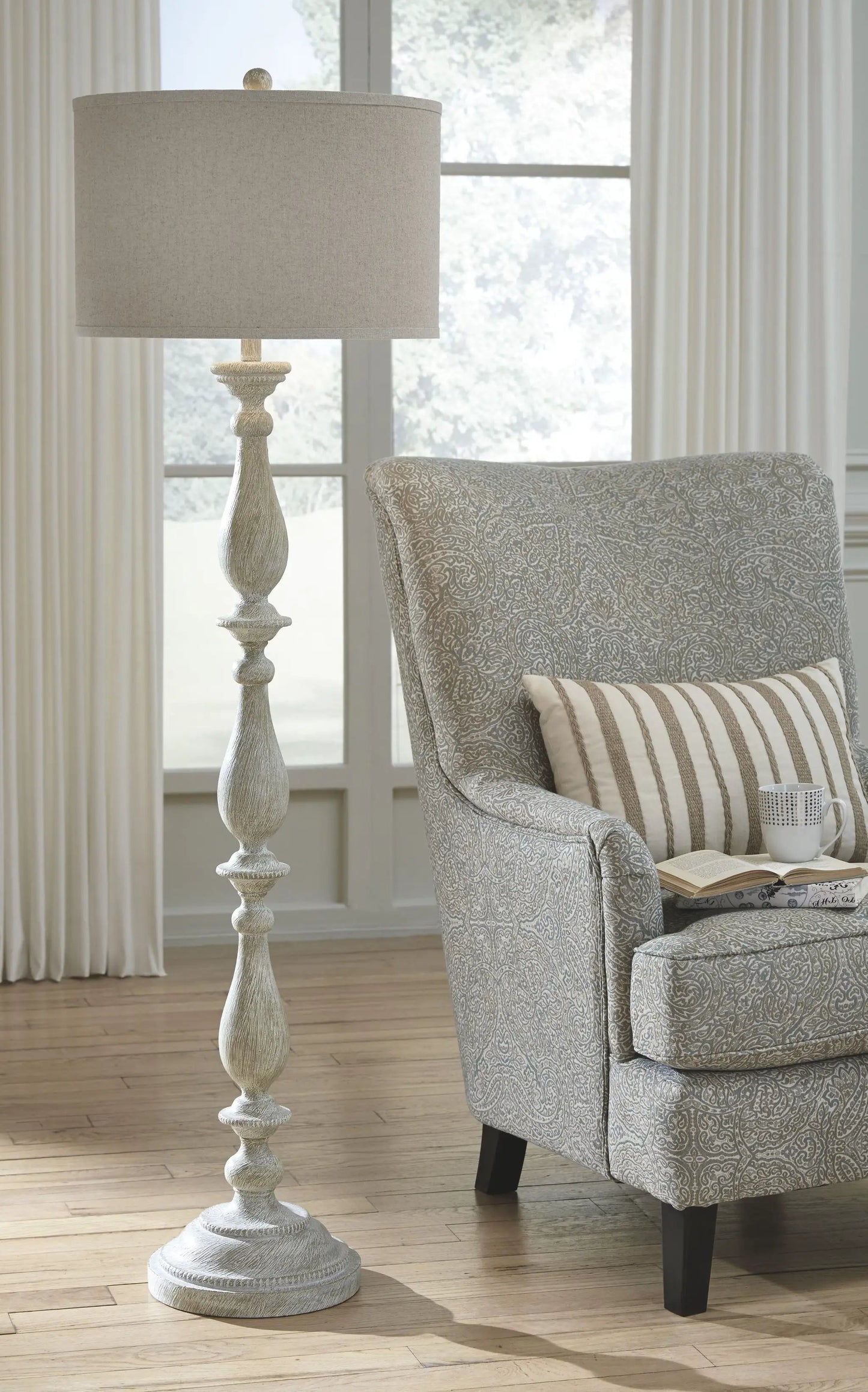Bernadate poly floor lamp whitewash finish with beige drum shade beside a patterned chair on Tampa Home & Garden Store