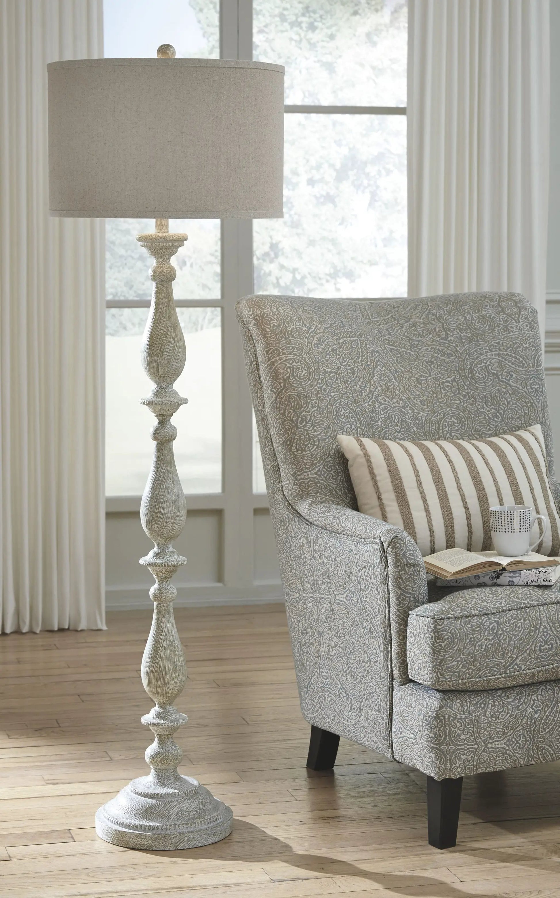 Bernadate poly floor lamp whitewash finish with beige drum shade beside a patterned chair on Tampa Home & Garden Store