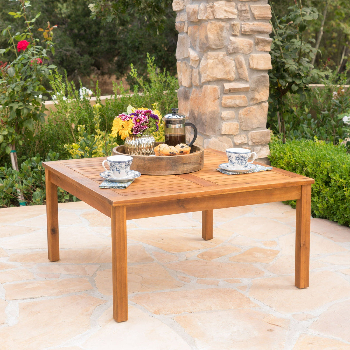 Perla Rustic Square Coffee Table with Block Legs in light brown wood on an outdoor stone patio on Tampa Home & Garden Store
