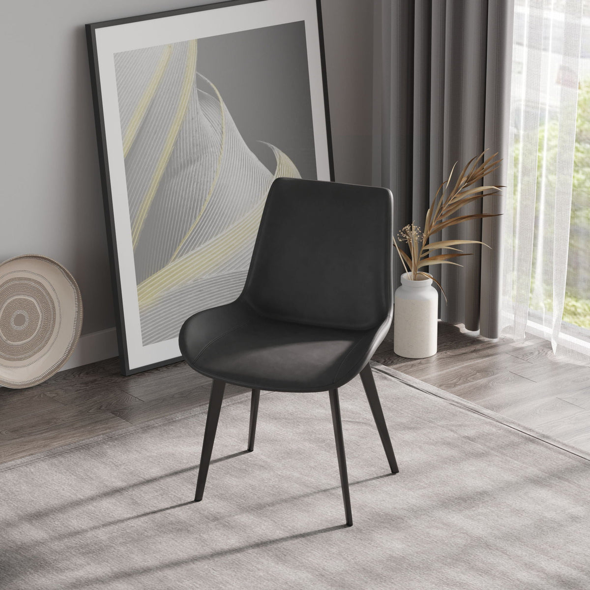 Modern dining chair with black faux leather seat and metal legs beside art in a living room on Tampa Home & Garden Store