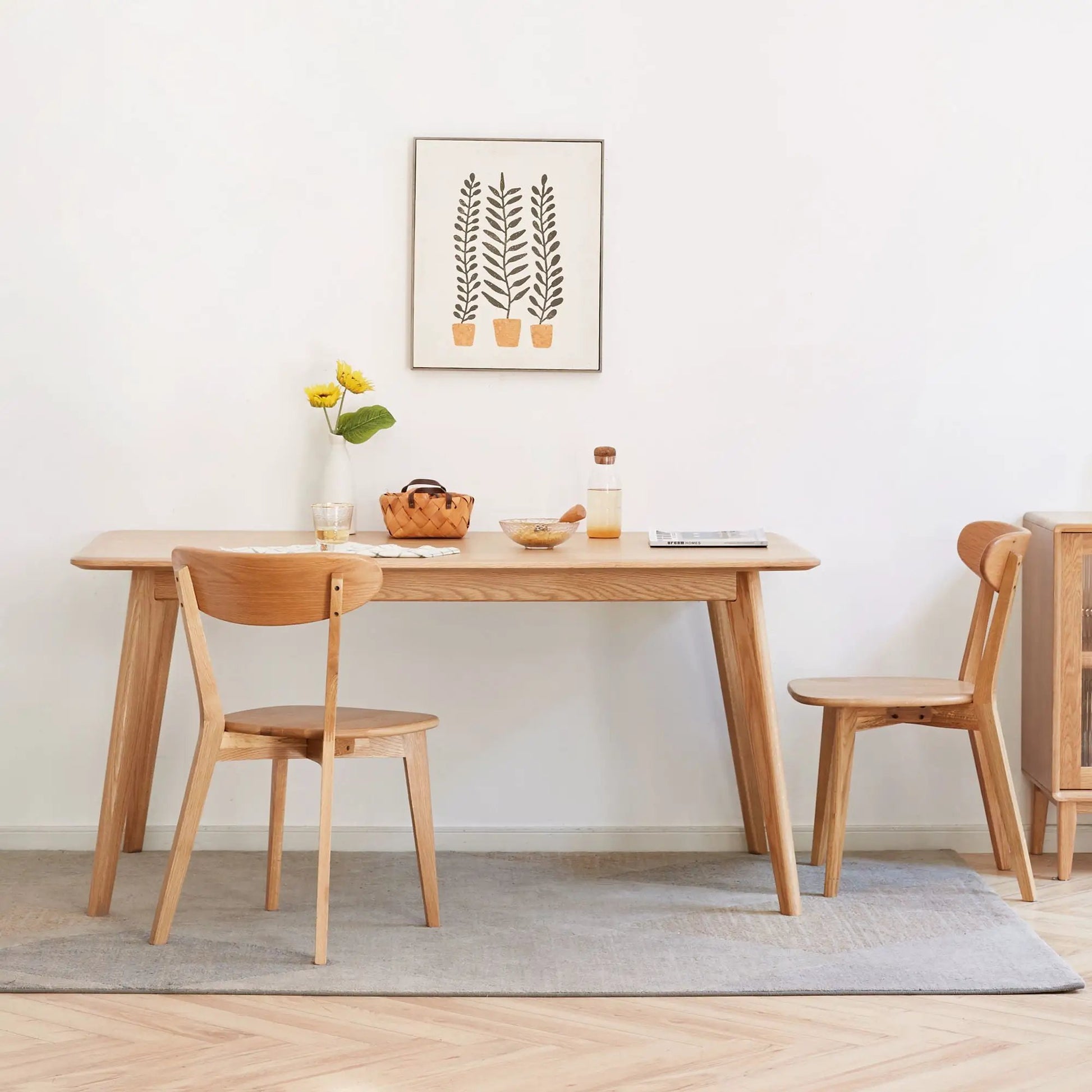 Simple dining chairs in natural wood around a light wooden dining table with wall art and a vase of flowers on Tampa Home & Garden Store