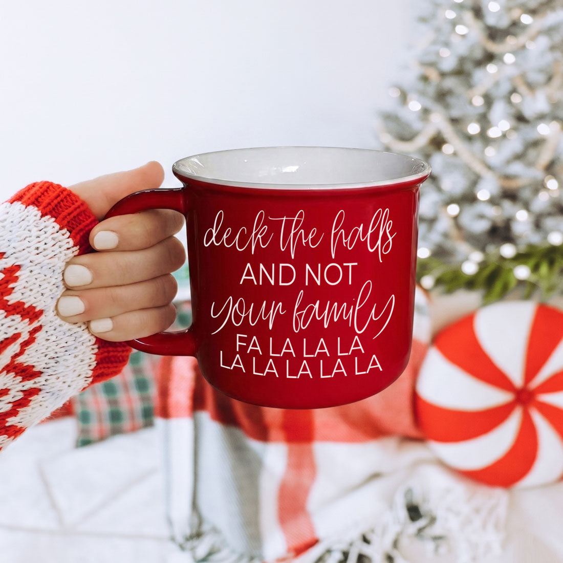 Coffee mug red Gia Roma deck the halls with white script held by hand near a Christmas tree on Tampa Home & Garden Store