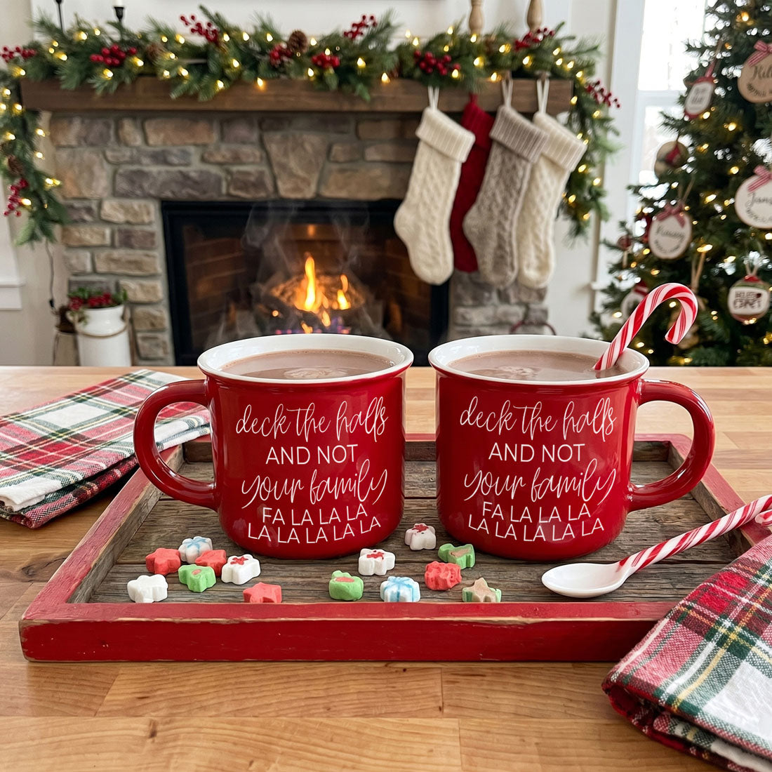 Pair of red Deck The Halls mugs with white script and candy cane on a wooden tray by a fireplace on Tampa Home & Garden Store