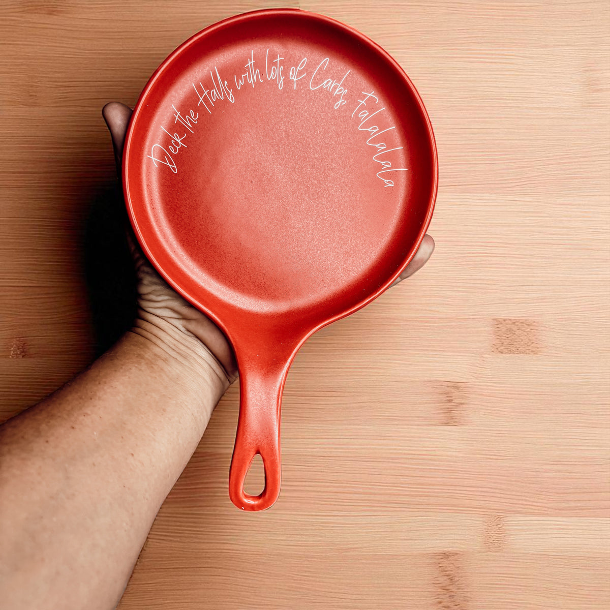 Gia Roma Deck the Halls & Carbs spoon rest, red enamel round with white script held in hand on Tampa Home & Garden Store