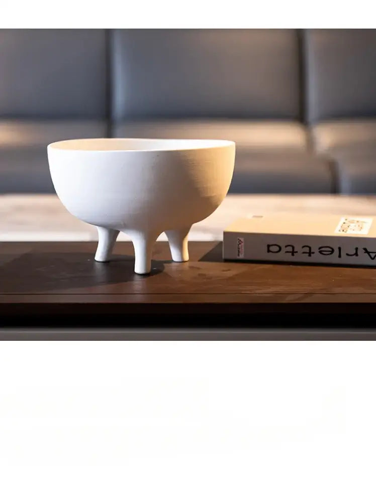 White ceramic tripod planter by Decorbites with three legs on dark wood table beside book on Tampa Home & Garden Store