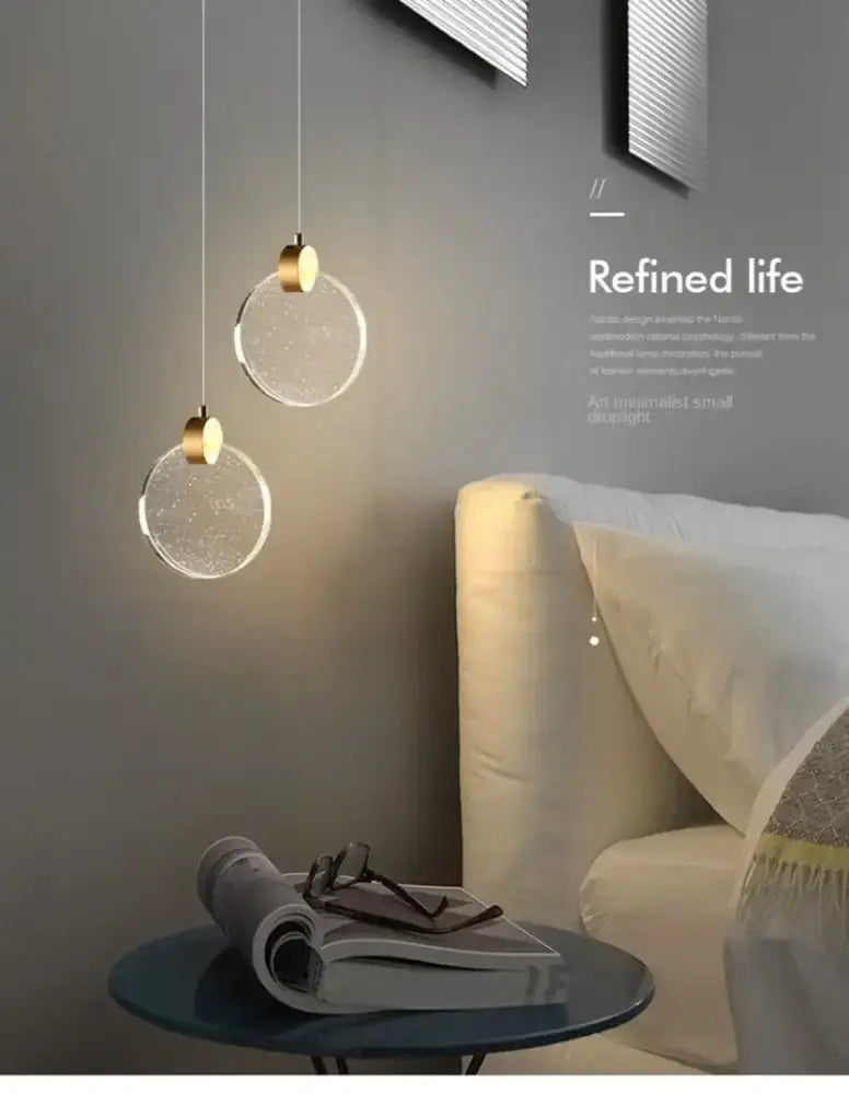 Two modern gold LED crystal pendant lights with glass discs over a bedroom nightstand on Tampa Home & Garden Store