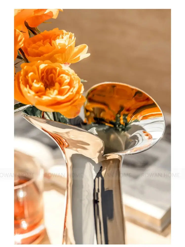 Vase silver stainless steel by Decorbites with a curved reflective neck and orange flowers on Tampa Home & Garden Store