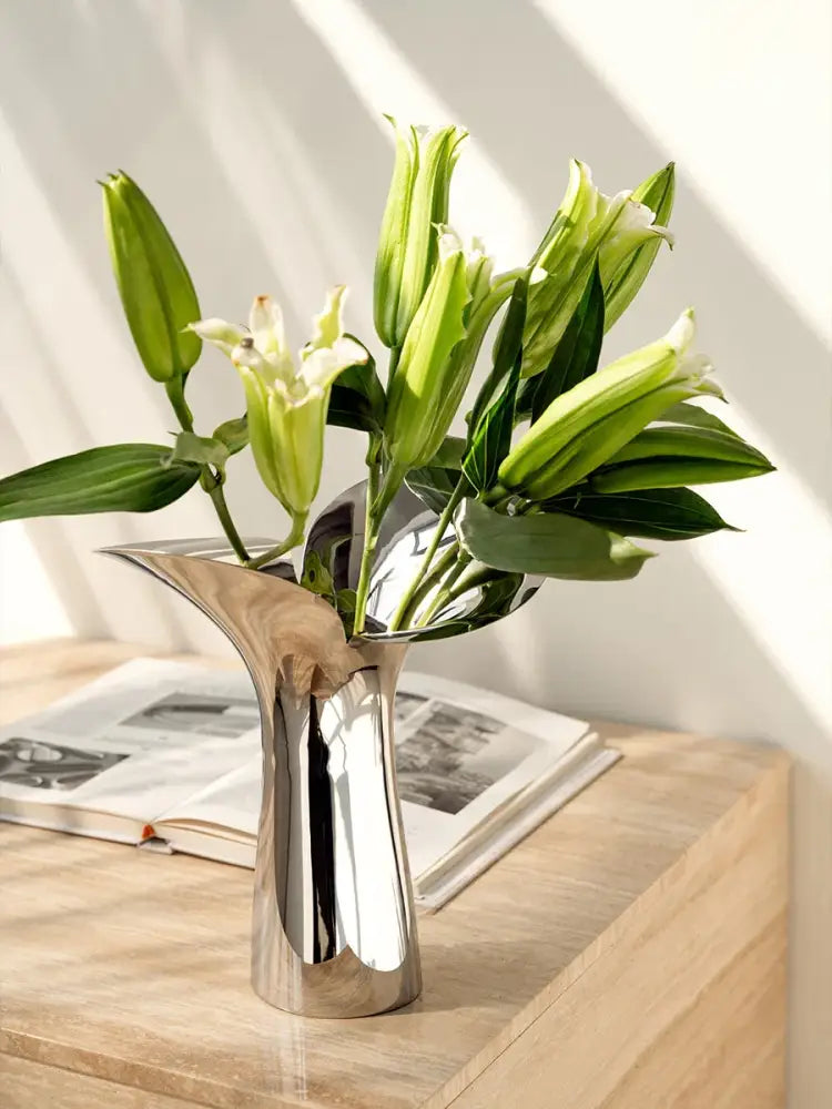 Silver stainless steel vase with curved silhouette holding white lilies on a wooden table on Tampa Home & Garden Store