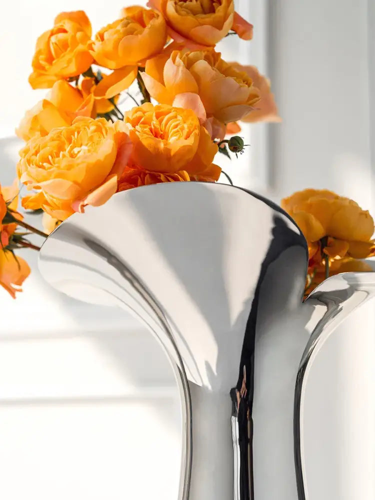 Silver stainless steel vase with curved, reflective surface holding orange roses on Tampa Home & Garden Store