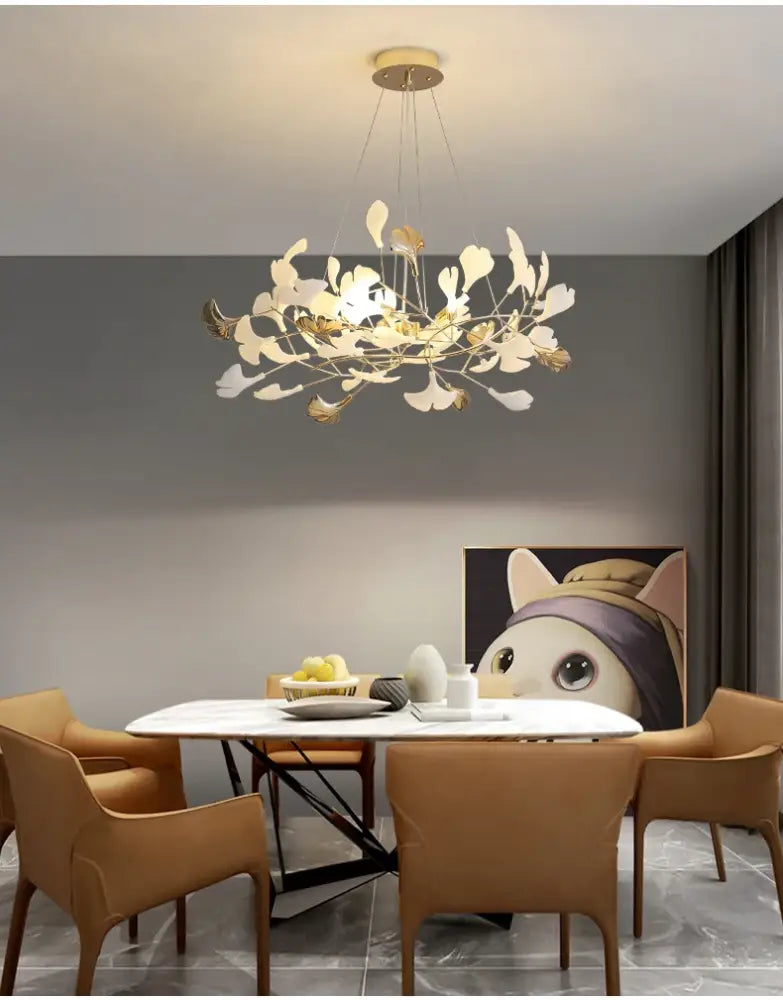 Decorbites Gold Ginkgo LED Chandelier with leaves over a round marble dining table and tan chairs on Tampa Home & Garden Store