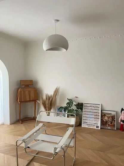 White dome pendant light with warm glow above a minimalist room and white metal chair on Tampa Home & Garden Store