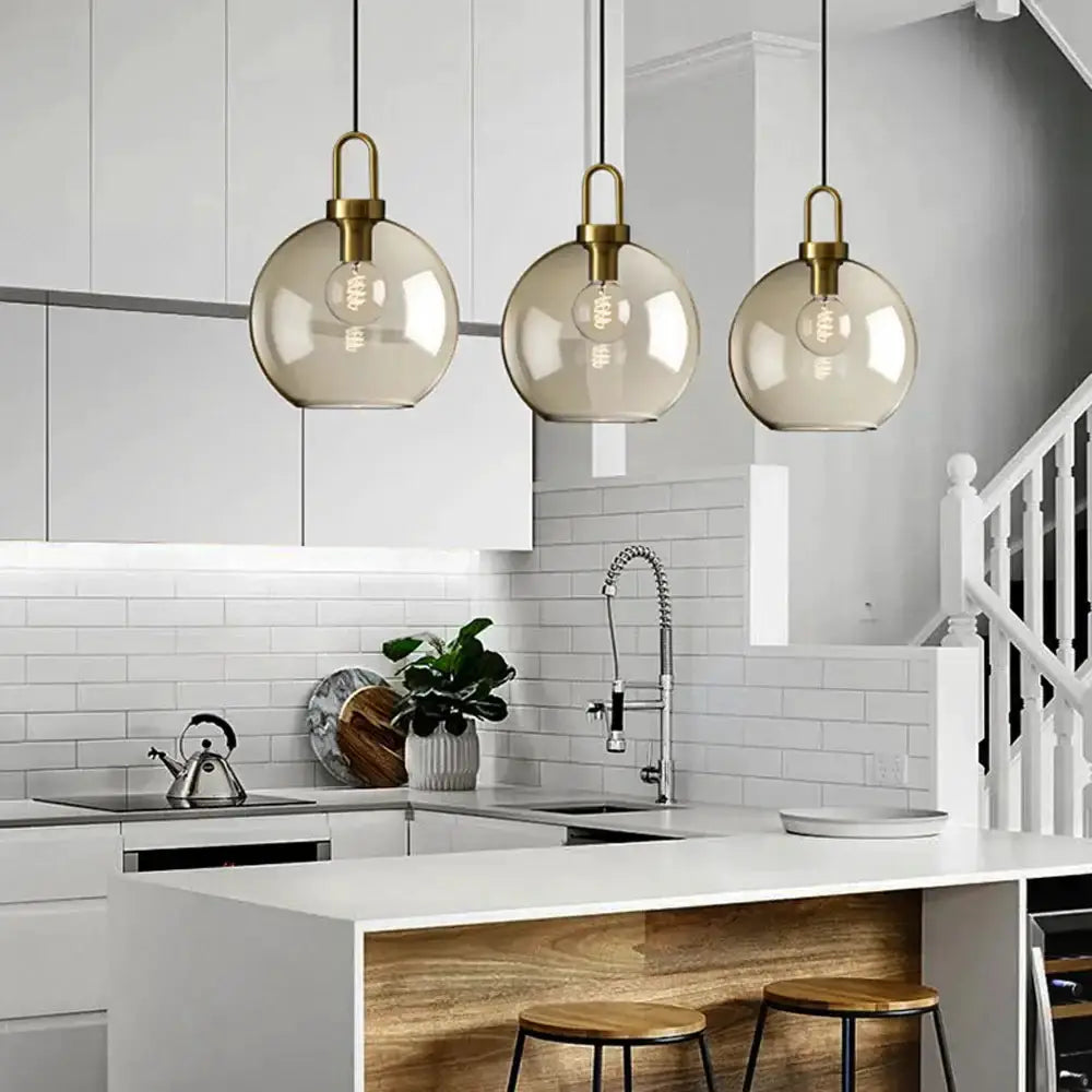 Pendant lights set with three smoked glass and brass fixtures over a white kitchen island on Tampa Home & Garden Store