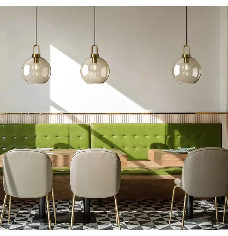 Modern smoked glass and brass pendant lights, set of 3, over a green banquette dining area on Tampa Home & Garden Store