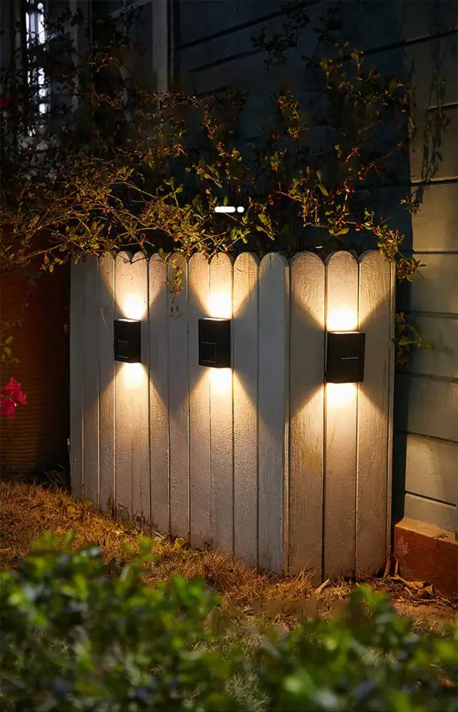 Three black Decorbites solar wall lights cast warm downward glow on a wooden fence on Tampa Home & Garden Store
