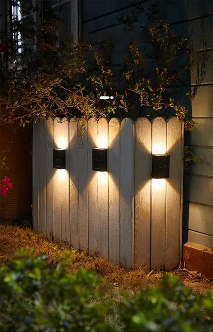 Three black Decorbites solar wall lights cast warm downward glow on a wooden fence on Tampa Home & Garden Store