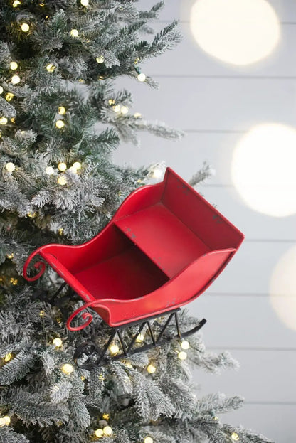 Red iron sleigh Christmas decoration on snow-dusted tree with warm lights on Tampa Home & Garden Store