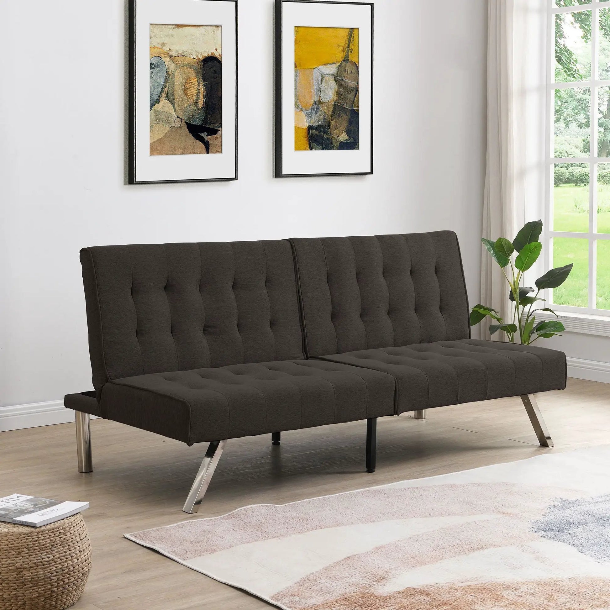 Futon sofa bed in dark charcoal with tufted cushions and metal legs; two wall artworks on Tampa Home & Garden Store